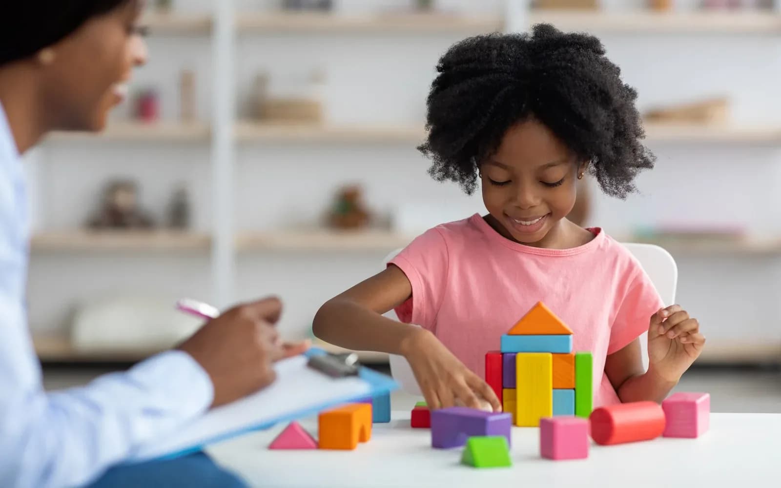A child building with colorful blocks while an adult observes and takes notes