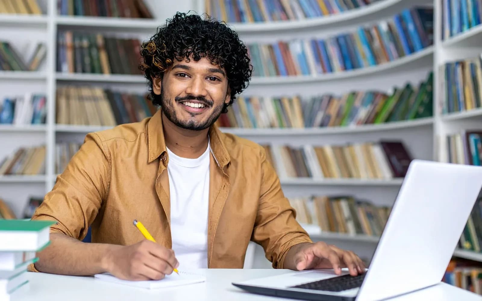 An adult studying with a notebook and laptop in a library